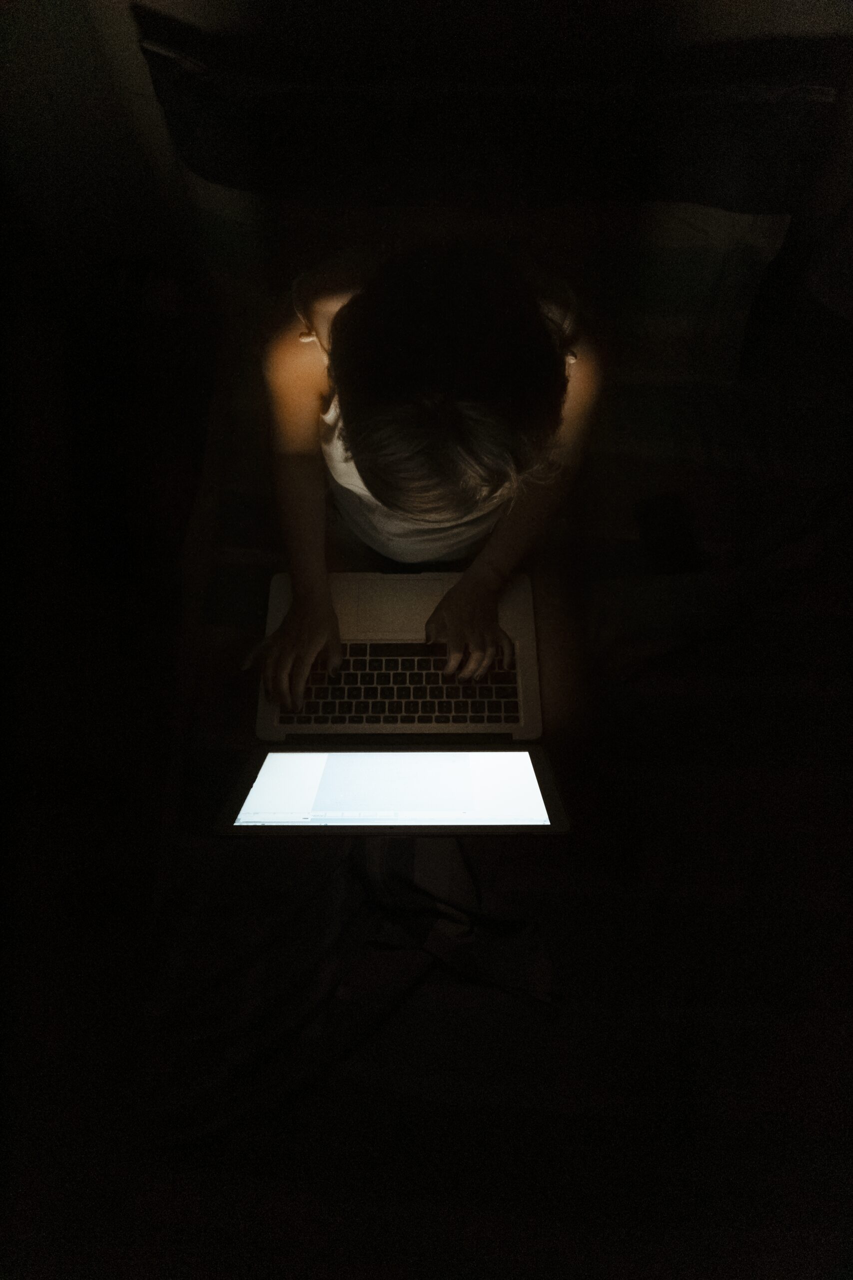 Vertical high angle shot of a female freelance worker sitting in a dark room typing on a laptop inteligência artificial